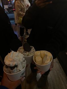 two cups of ice cream with whipped cream and chocolate on top are being held by people