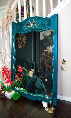 a blue mirror sitting on top of a wooden floor next to a vase filled with flowers