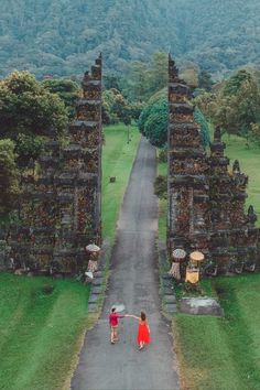 two people are walking down the road in front of some statues