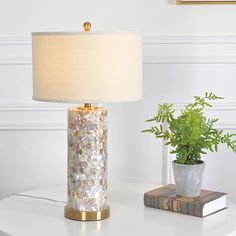 a white table with a lamp and a potted plant on it next to a book