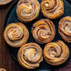 several cinnamon rolls on a black plate with powdered sugar around them and two wooden spoons