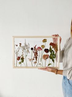 a woman holding up a framed photo with wildflowers in the frame on it