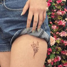 a woman's thigh with a small tattoo on her left leg and flowers in the background