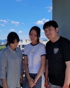 three people standing next to each other on a balcony with buildings in the background and blue sky