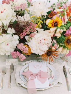 the table is set with pink and white flowers, silverware, and napkins