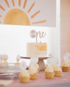 a cake and cupcakes on a table with the sun in the sky behind it