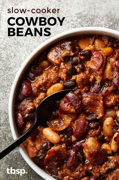 a bowl filled with meat and beans sitting on top of a table next to a spoon