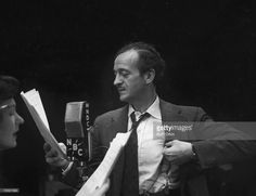 a man in a suit and tie standing next to a woman holding papers while talking into a microphone