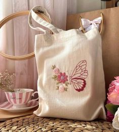 a white bag sitting on top of a table next to pink flowers and a cup