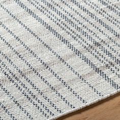 a white rug with blue and grey stripes on top of a wooden floor next to a wood floor