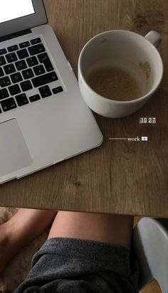 a laptop computer sitting on top of a wooden table next to a cup of coffee