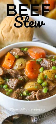 beef stew in a white bowl with carrots, peas and bread on the side