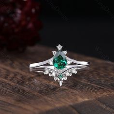 an engagement ring with a green stone surrounded by white diamonds on top of a wooden table