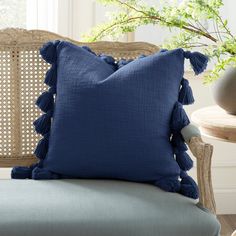 a blue pillow sitting on top of a chair next to a vase with green plants