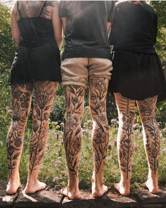 three people with tattoos on their legs standing in front of some trees and flowers,