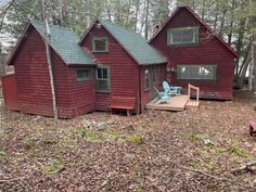 a red cabin in the woods with two chairs and a deck on the front porch