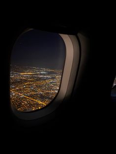 an airplane window with the view of city lights at night from it's wing