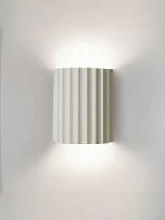 a white wall light mounted on the side of a wall next to a lamp shade