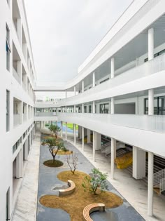 an empty courtyard with benches and trees in the foreground, surrounded by white buildings