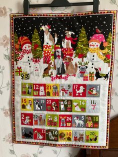 a quilted calendar hanging on the wall with dogs and snowmen around it's edges