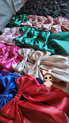 many different colors of satin bows on the floor with a small doll in the middle