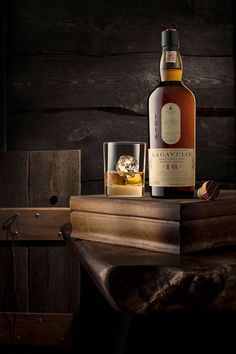 a bottle of whisky sitting on top of a wooden table next to a glass filled with ice