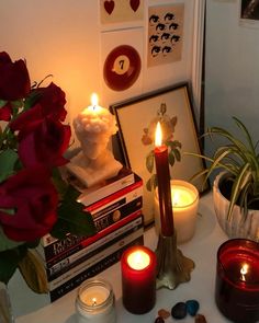 some candles are sitting on a table next to books and pictures with roses in them