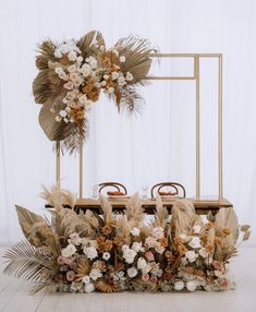 an arrangement of flowers and plants on a table with a gold frame in the background