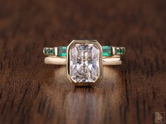 an engagement ring with a large white diamond surrounded by green emeralds on a wooden surface