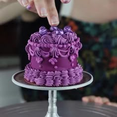 a purple cake is being held by a person's hand on a silver platter