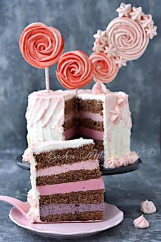 a slice of cake with pink and white frosting on a plate next to two lollipops