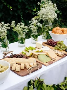 a table topped with cheeses, grapes and crackers next to vases filled with flowers