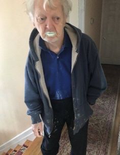 an old man with a toothbrush in his mouth standing next to a rug on the floor