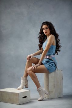 a young woman sitting on top of a box posing for a photo in front of a gray background