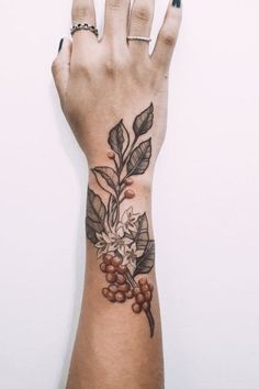 a woman's hand with a flower and leaves tattoo on her left arm,