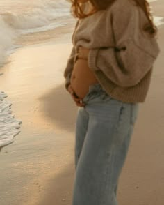 a woman standing on top of a beach next to the ocean with her stomach exposed