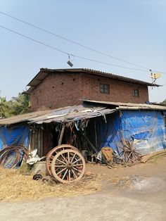 an old wooden wheel sits in front of a building with blue tarps on it