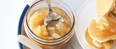 a plate with pancakes and butter on it next to a jar of jam, spoon