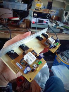 a person holding up a piece of electronic equipment in their hand, with other electronics on the table behind them