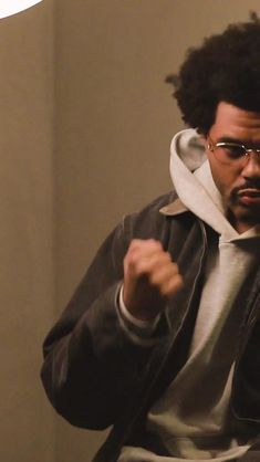 a man wearing glasses and a hoodie is holding his fist up