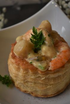 there is a small pastry with shrimp and sauce in it on a white plate next to some parsley