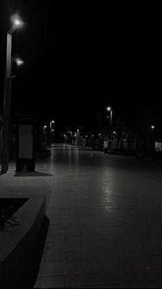 a person sitting on a bench in the middle of a sidewalk at night with street lights