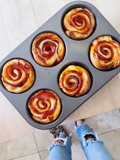 a person standing next to a muffin pan filled with pastries