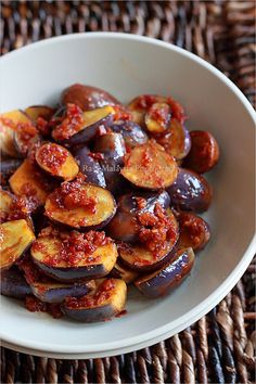 a white bowl filled with cooked eggplant on top of a woven table cloth