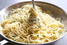 a fork is stuck into some noodles in a silver bowl with parsley on top