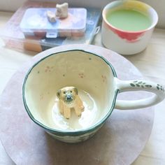 a dog figurine sitting in a mug on a table next to a cup of green tea