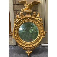 an ornate gold mirror on the ground in front of a building with a statue of an eagle