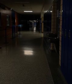 an empty hallway leading to lockers in a dark room with light coming from the ceiling