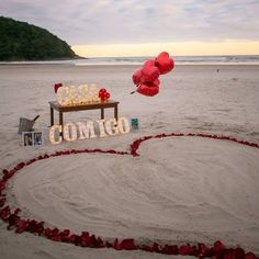 a heart shaped sign on the beach with balloons