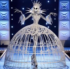 a woman in a white dress standing on top of a stage with an open birdcage